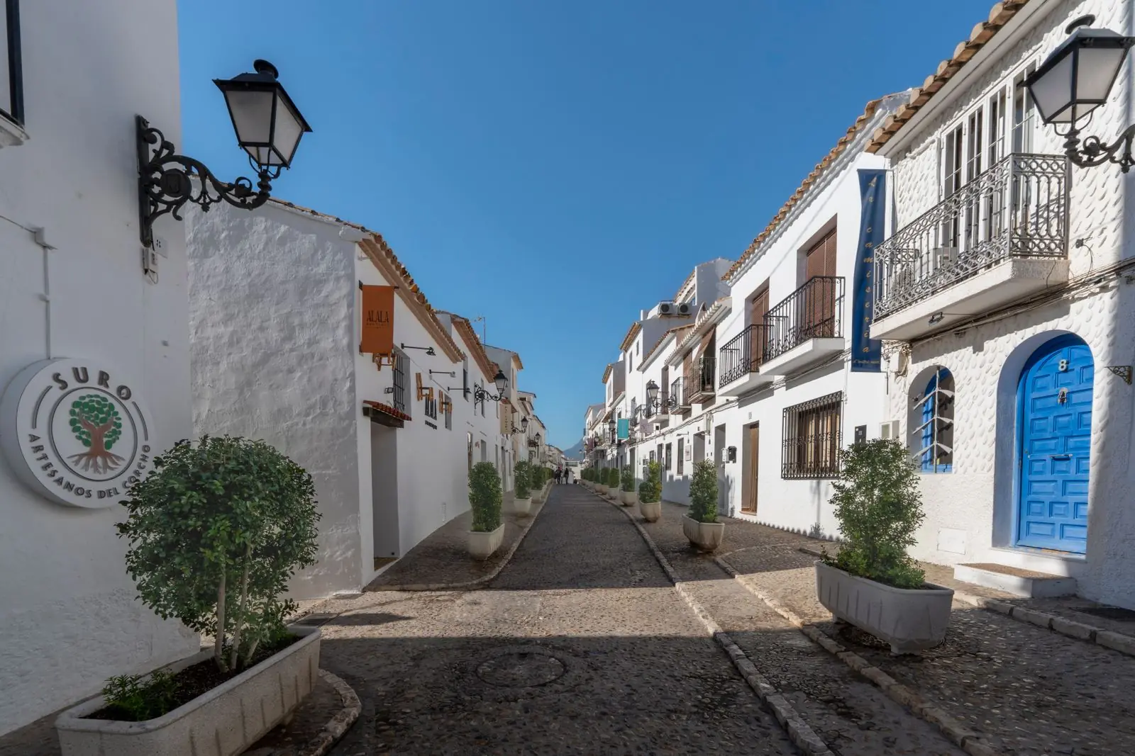 Wit geschilderde straat met keien en lantaarns in Altea