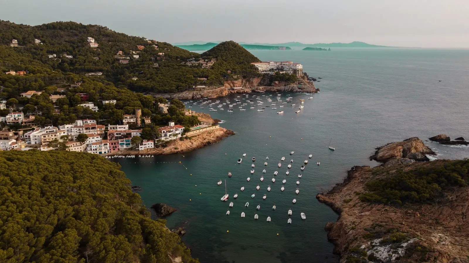 Luchtfoto van de baai Sa Tuna met bootjes, huizen en groene heuvels