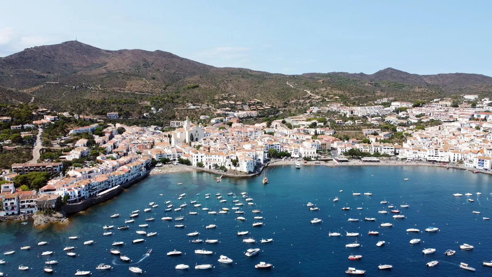 Luchtfoto van Cadaqués met witte huizen rond een baai vol boten