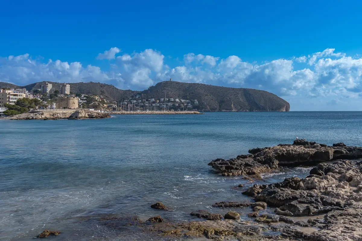 Rotsachtige kust bij Moraira met heldere zee en bergen op de achtergrond