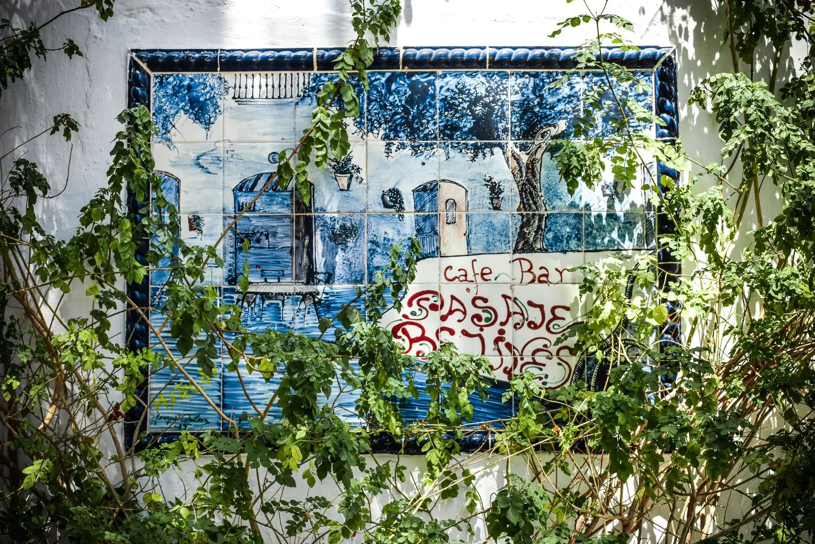 Muurschildering van een Spaans café tussen groene planten in Estepona
