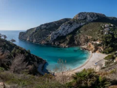 Kleine baai met helder turquoise water omringd door beboste kliffen bij Jávea