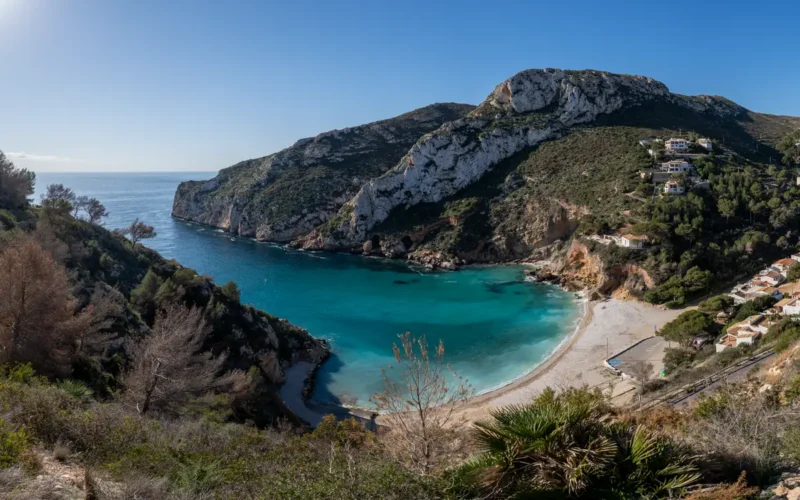 Kleine baai met helder turquoise water omringd door beboste kliffen bij Jávea