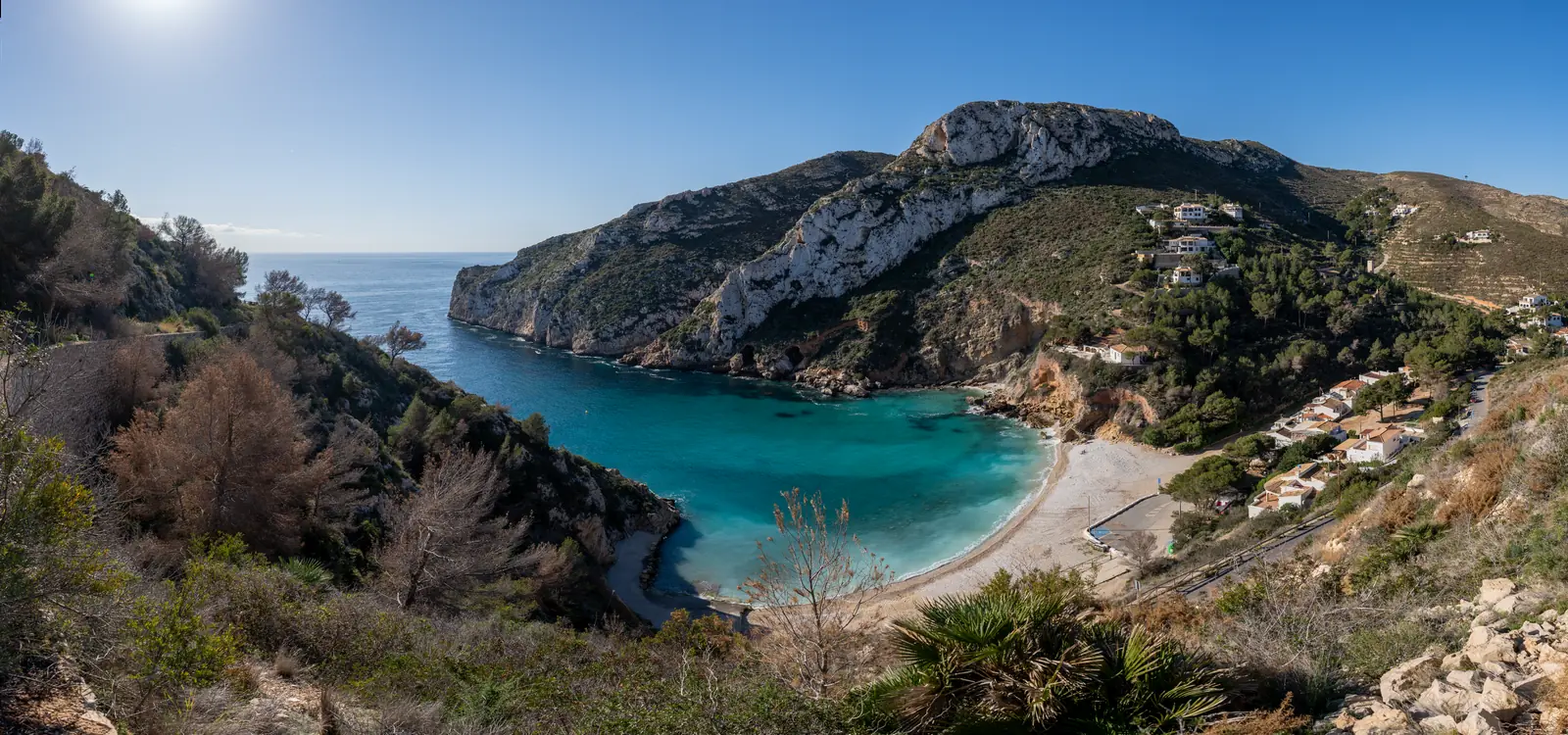 Kleine baai met helder turquoise water omringd door beboste kliffen bij Jávea