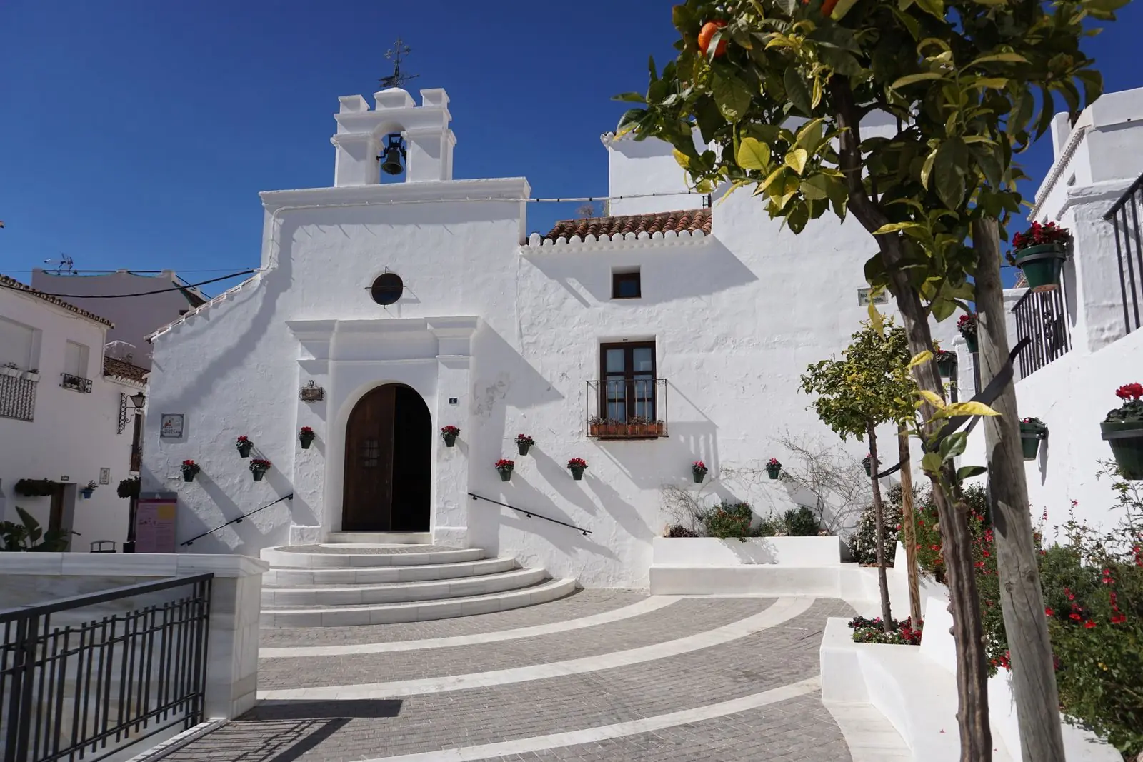 Witte kerkgevel met trappen en een klokje in Mijas