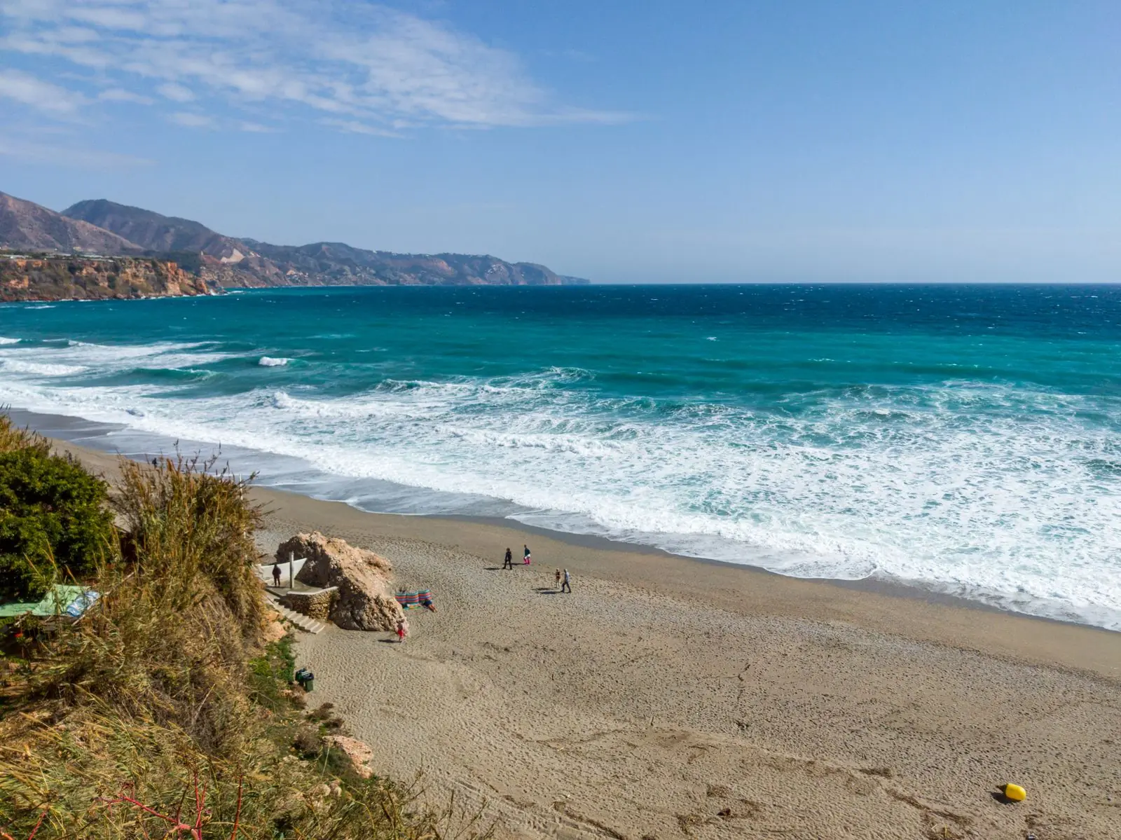 Breed zandstrand bij Nerja met golven en kliffen op de achtergrond