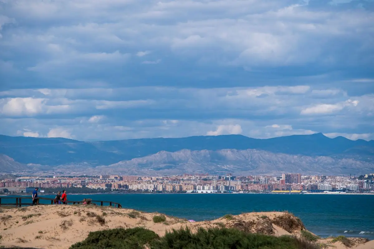 Zandduinen en zee met de stad Alicante en bergen op de achtergrond