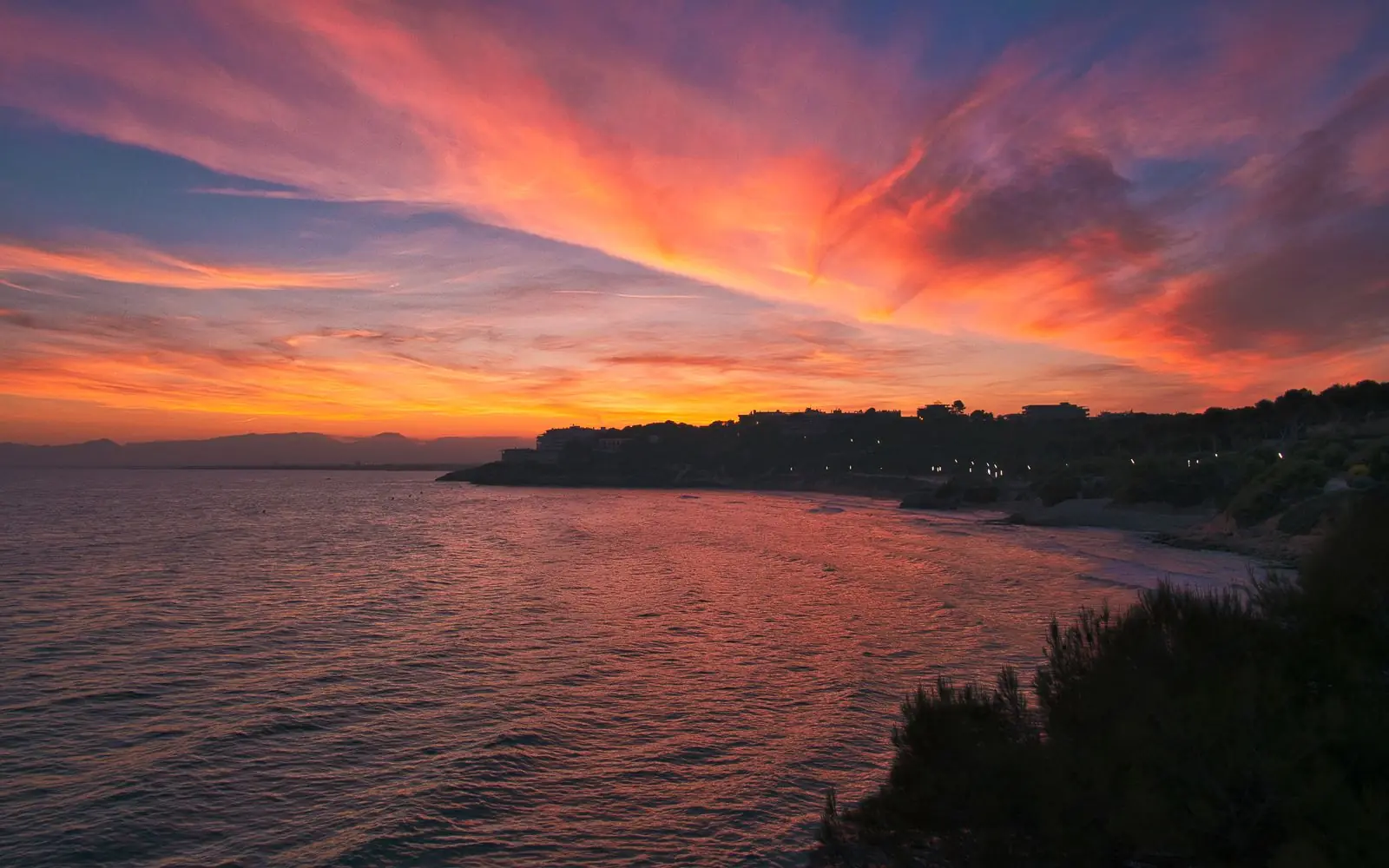 Rode avondlucht boven de rotsachtige kust van Salou